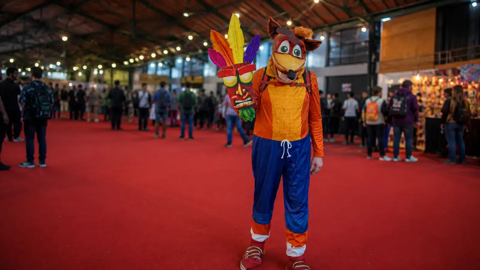Cosplayer de Crash Bandicoot con una máscara de Aku Aku en una convención de videojuegos.