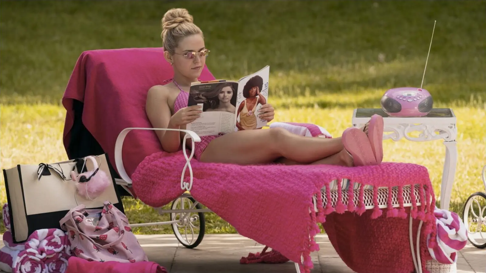 Lexi Minetree como Elle Woods lee una revista en una silla rosa junto a un radio portátil.