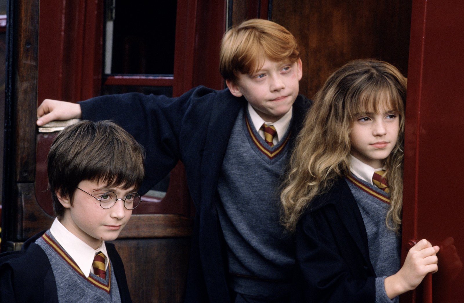 Harry, Ron and Hermione in school uniforms beside the Hogwarts Express in the first Harry Potter film
