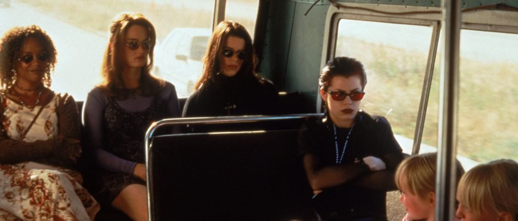 The four young witches from The Craft sitting together on a bus wearing sunglasses