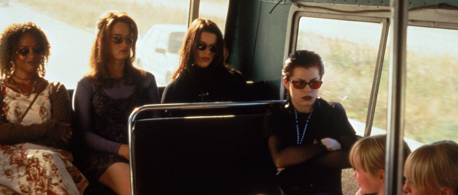 The four young witches from The Craft sitting together on a bus wearing sunglasses